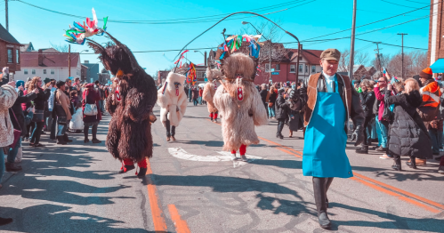 Colorful parade scene with costumed performers and a crowd watching on a sunny day.