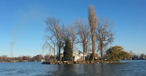 A small island with a house and trees surrounded by calm water under a clear blue sky.