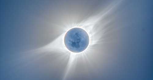 A stunning solar eclipse with the moon partially covering the sun, surrounded by radiant solar flares and a blue sky.