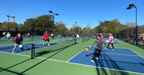 A lively pickleball game in progress on outdoor courts, with players of various ages enjoying the sunny day.