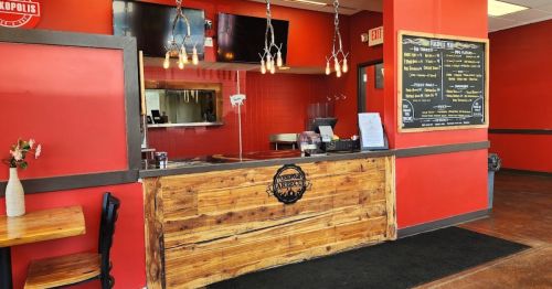 A rustic restaurant counter with a wooden design, red walls, and a menu board, featuring hanging light fixtures.