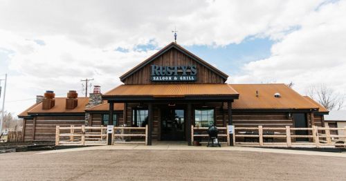Exterior of Rusty's Saloon & Grill, featuring a wooden facade and a metal roof under a cloudy sky.