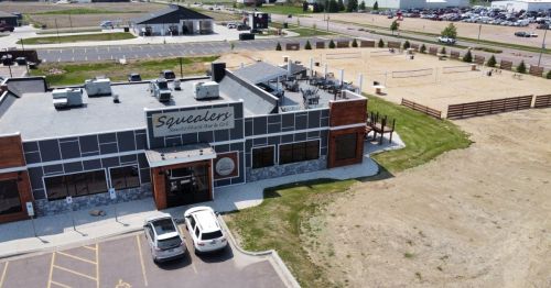 Aerial view of Squealers BBQ restaurant with outdoor seating and a sandy volleyball court nearby.