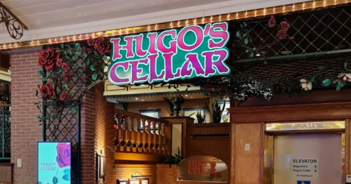 Sign for "Hugo's Cellar" adorned with roses, located in a brick-walled restaurant setting.