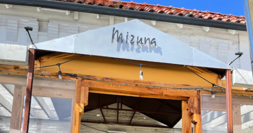 Sign for "Mizuna" above a wooden entrance, with string lights and a clear blue sky in the background.