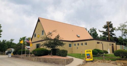 A building with a copper-colored roof, surrounded by greenery and flags, with a sign in front.