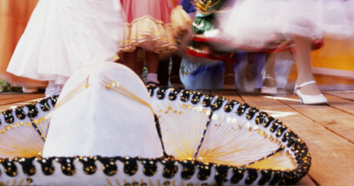 A colorful sombrero in the foreground with dancers in traditional attire twirling in the background.