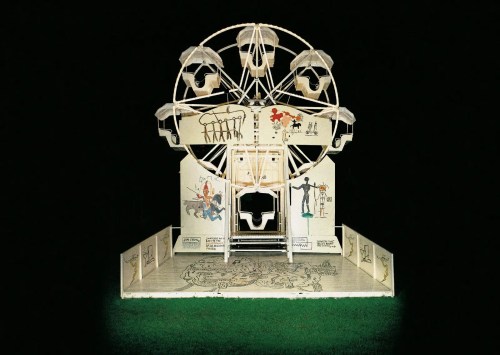 A whimsical, illuminated Ferris wheel model with cartoonish figures and drawings, set against a dark background.