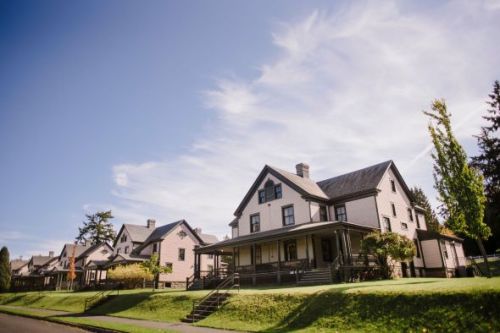 A row of charming, two-story houses with porches, set against a clear blue sky and green lawns.