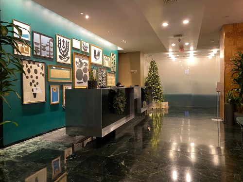 Modern lobby with green walls, framed artwork, a sleek reception desk, and a small Christmas tree in the corner.