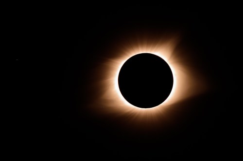 A solar eclipse with a dark circle surrounded by a glowing halo of light against a black background.
