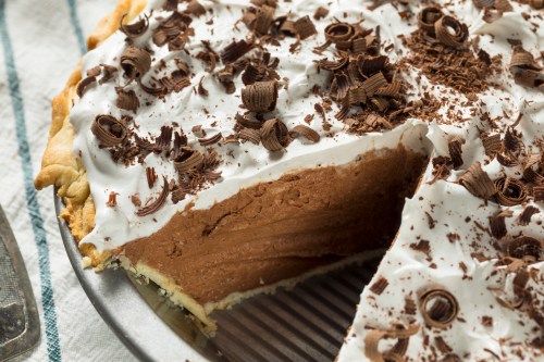 A chocolate cream pie topped with whipped cream and chocolate shavings, with a slice cut out.