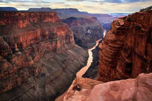 A breathtaking view of the Grand Canyon, showcasing steep red cliffs and a winding river below under a cloudy sky.