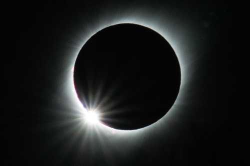 A solar eclipse with a darkened sun surrounded by a glowing halo and radiant light beams.