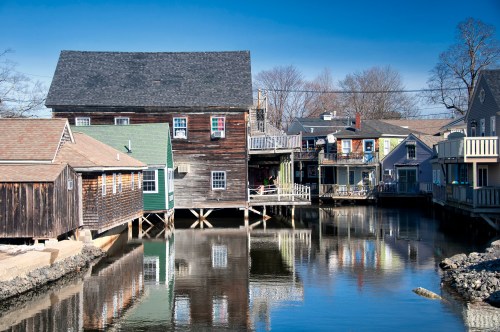A scenic view of colorful buildings along a calm waterway, reflecting the structures under a clear blue sky.