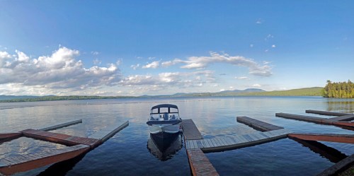 A serene lake scene with a boat docked at wooden piers under a clear blue sky and distant mountains.