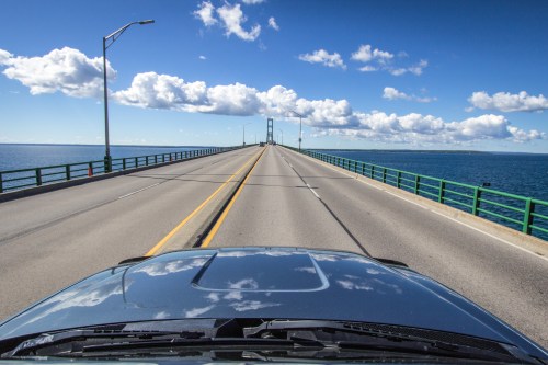 View from a vehicle approaching a bridge over water, with blue skies and scattered clouds above.