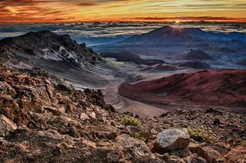 A stunning sunset over a volcanic landscape, with rocky terrain and clouds in the distance.