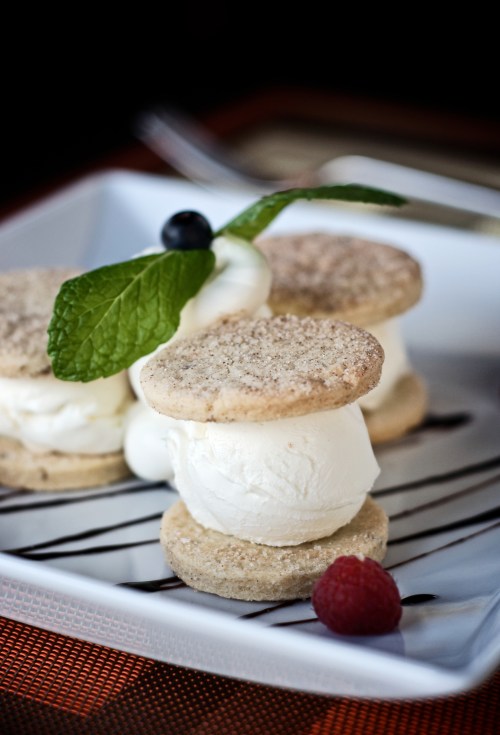 Two ice cream sandwiches with vanilla ice cream, topped with a mint leaf, a blueberry, and a raspberry on a plate.
