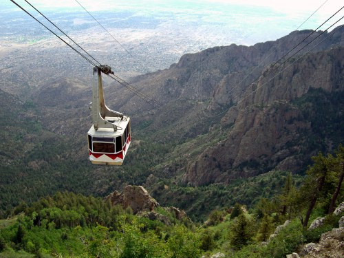 A cable car glides over a mountainous landscape, surrounded by greenery and rocky terrain.