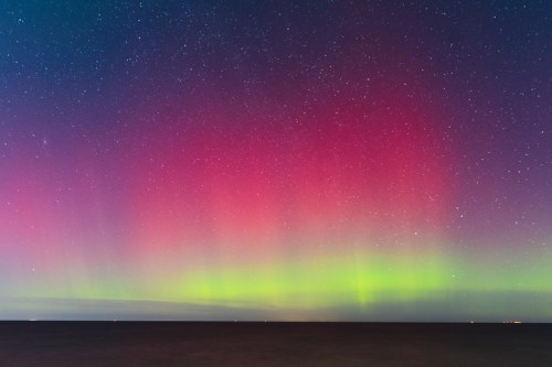 A vibrant aurora borealis lights up the night sky with shades of pink and green over a calm sea. Stars twinkle above.