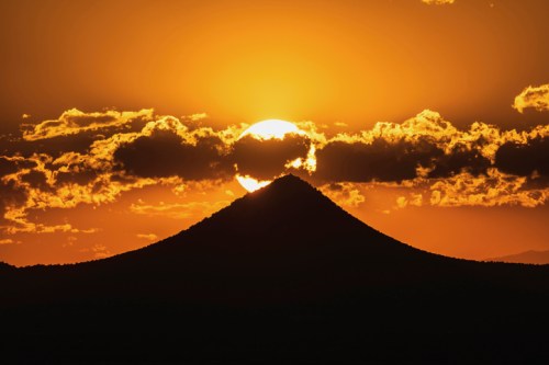 Sunset behind a silhouette of a mountain, with vibrant orange and yellow hues illuminating the sky and clouds.
