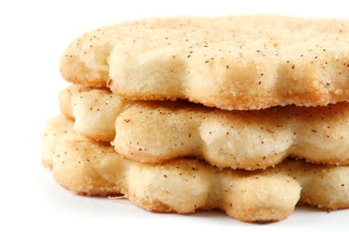 Three stacked, lightly golden-brown cookies with a textured surface, sprinkled with a hint of cinnamon.
