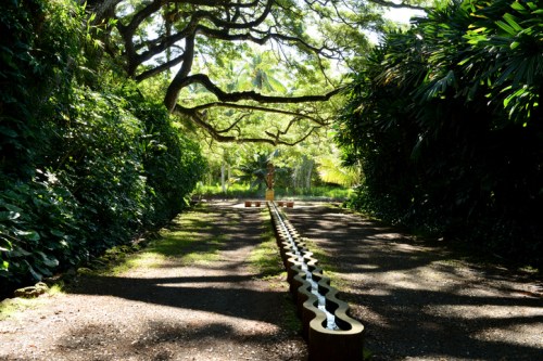 A serene garden path lined with lush greenery and a decorative water feature under a canopy of trees.