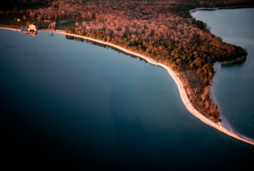 Aerial view of a serene coastline with sandy beaches and lush trees along a calm blue lake at sunset.