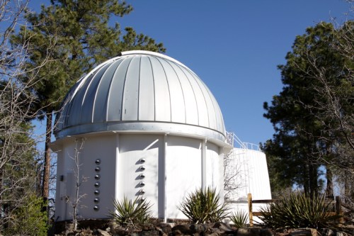 A white observatory dome surrounded by trees under a clear blue sky.