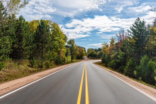 A winding road surrounded by lush green trees under a partly cloudy sky.