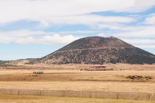 A grassy landscape with a prominent mountain in the background under a partly cloudy sky.