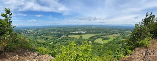 Panoramic view of lush green hills and fields under a partly cloudy sky from a high vantage point.