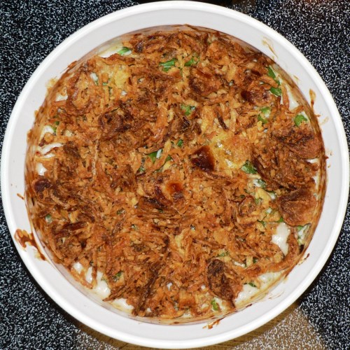 A baked casserole topped with crispy fried onions, featuring a creamy filling and green vegetables.