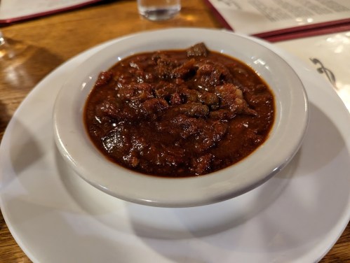 A bowl of hearty chili with chunks of meat and beans, served on a white plate.