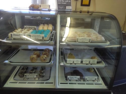Display case filled with various baked goods, including cupcakes, cookies, and cinnamon rolls.
