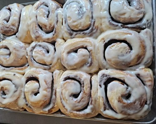 A tray of freshly baked cinnamon rolls topped with creamy icing, arranged in a neat pattern.