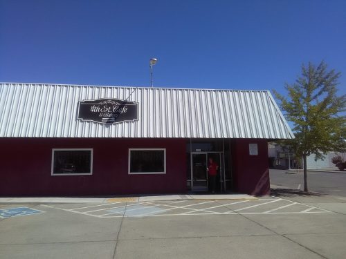 Exterior of a café with a metal roof, featuring a sign that reads "5th St Café & Bakery" and a person at the entrance.