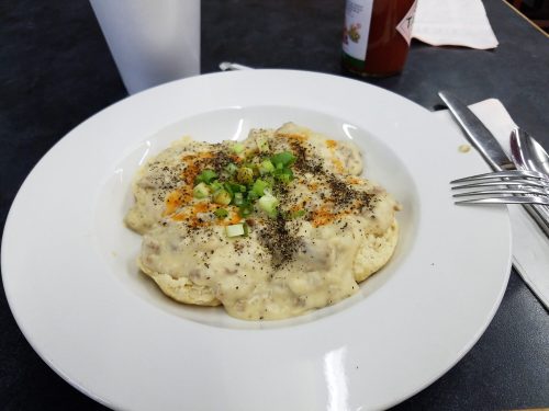 A plate of biscuits topped with creamy sausage gravy, sprinkled with green onions and black pepper.