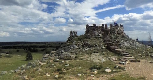 A stone structure atop a rocky hill, surrounded by grassy fields and under a cloudy sky.