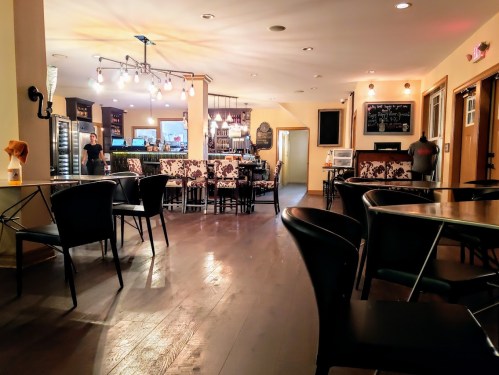 A cozy café interior with black chairs, a bar area, and warm lighting, creating an inviting atmosphere.