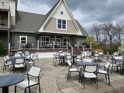 Outdoor seating area with empty tables in front of a large, modern building under a cloudy sky.