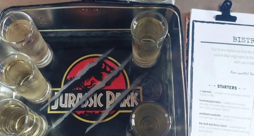 A tray with shot glasses and a "Jurassic Park" logo, alongside a bistro menu featuring various food options.