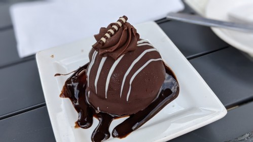 A chocolate dessert dome with a swirl of frosting and drizzled chocolate sauce on a white plate.