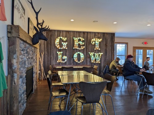 A cozy restaurant interior featuring a "GET LOW" sign, wooden walls, and patrons seated at tables.