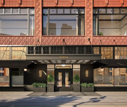 Exterior view of a stylish building with red brick detailing and large windows, featuring the name "Shinola" above the entrance.