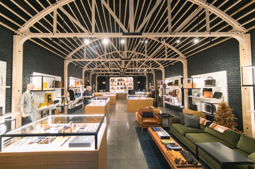 A modern retail space with wooden beams, showcasing various products in display cases and a cozy seating area.