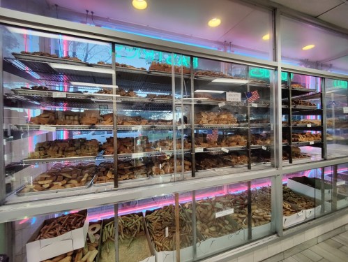 A display case filled with various baked goods, including cookies, pastries, and bread, illuminated by neon lights.
