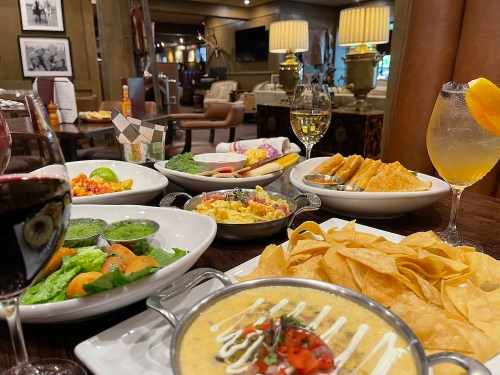 A table set with various dishes, including nachos, salads, and drinks, in a cozy restaurant setting.