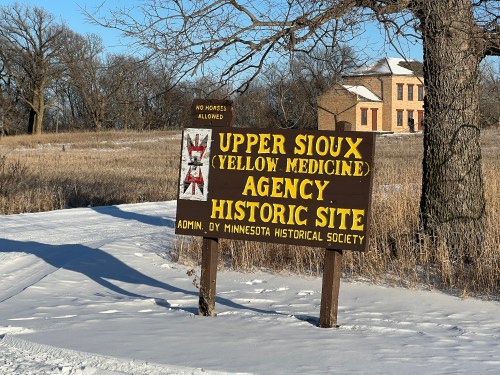 Sign for Upper Sioux Agency Historic Site, featuring yellow and red text, surrounded by snow and a field.